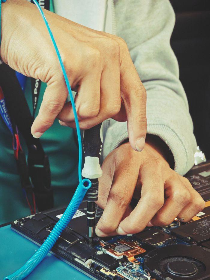Manos reparando el interior de una notebook abierta con un destornillador de precisión